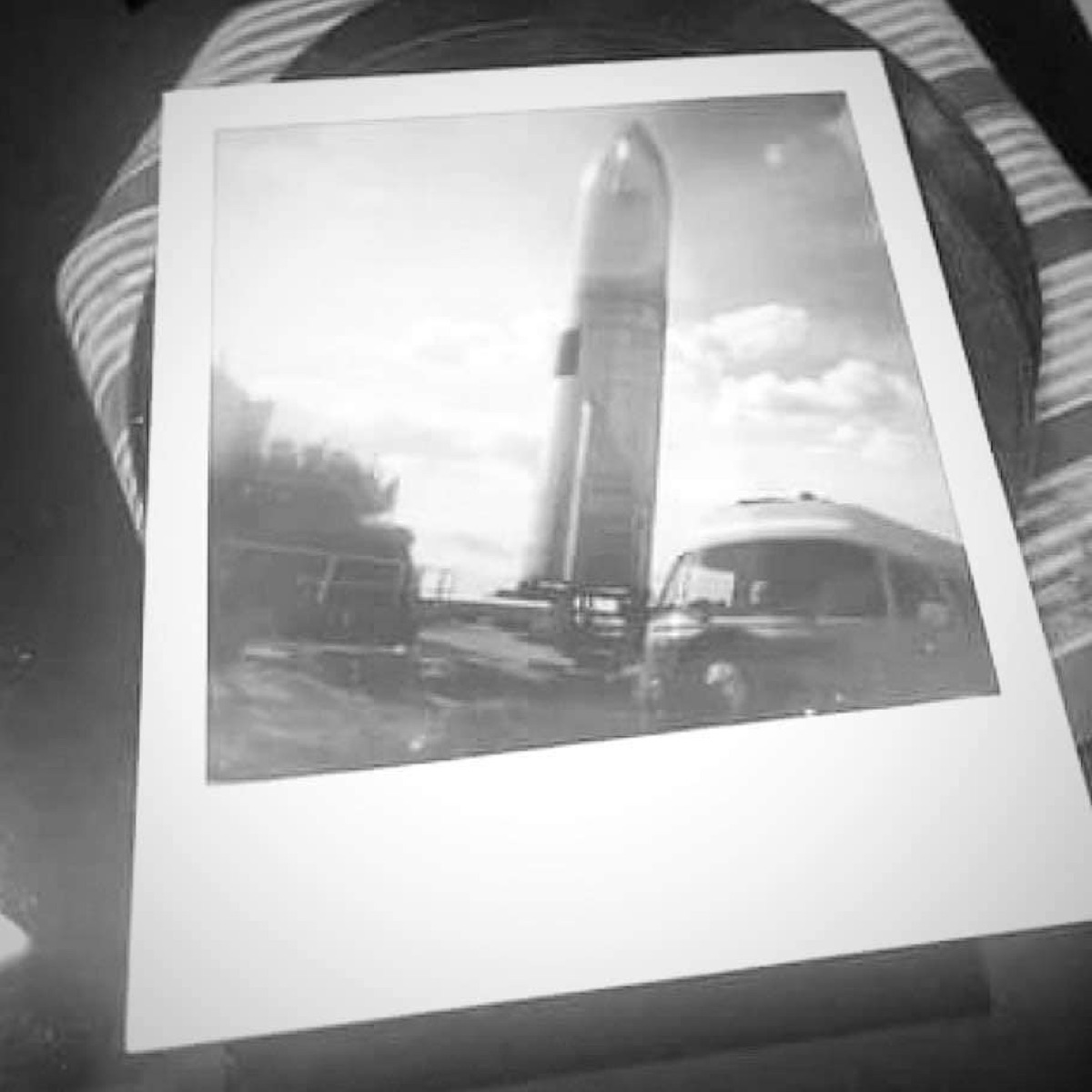 A scanned Polaroid of a Bus beneath a tall rocket